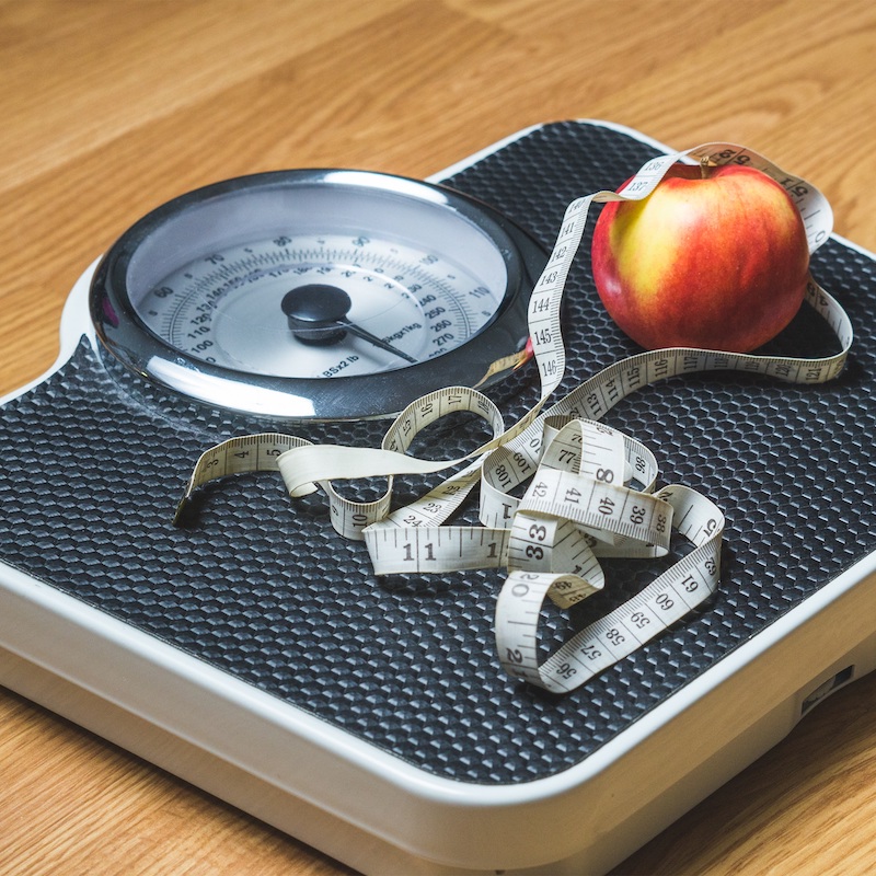 A red apple and measuring tape placed on a set of weighing scales