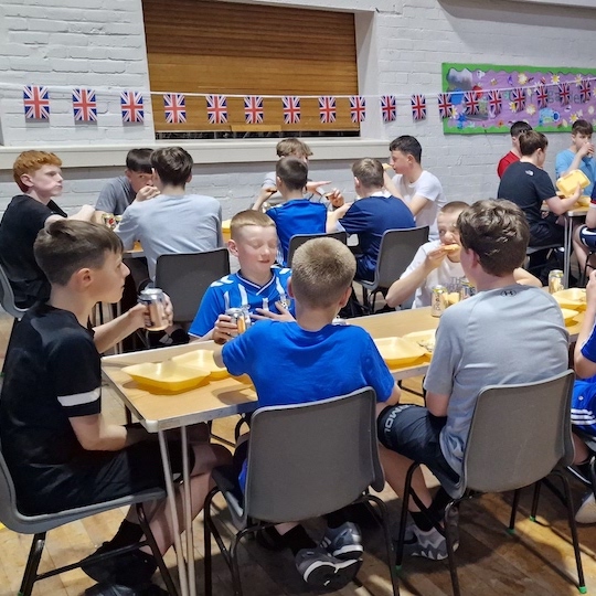 Members of Boys Brigade sitting around tables eating and talking