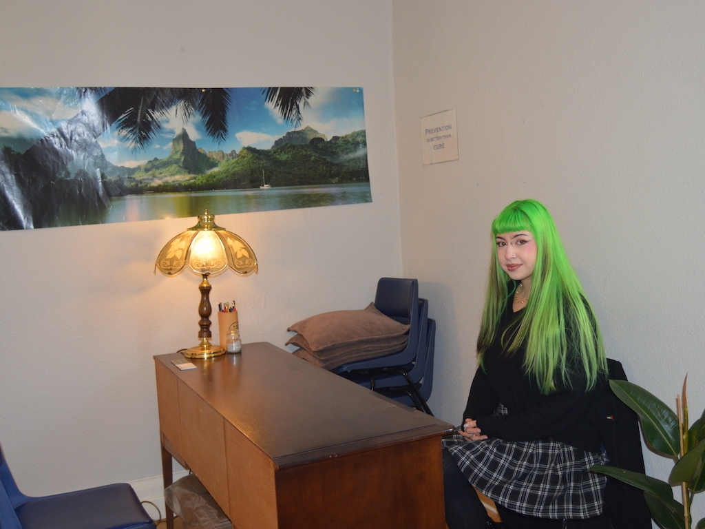 Young woman with long green hair sitting behind desk