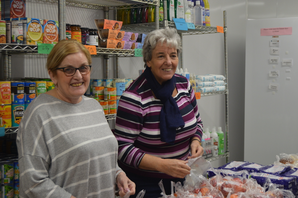 Two female staff working at the Larder surrounded by groceries